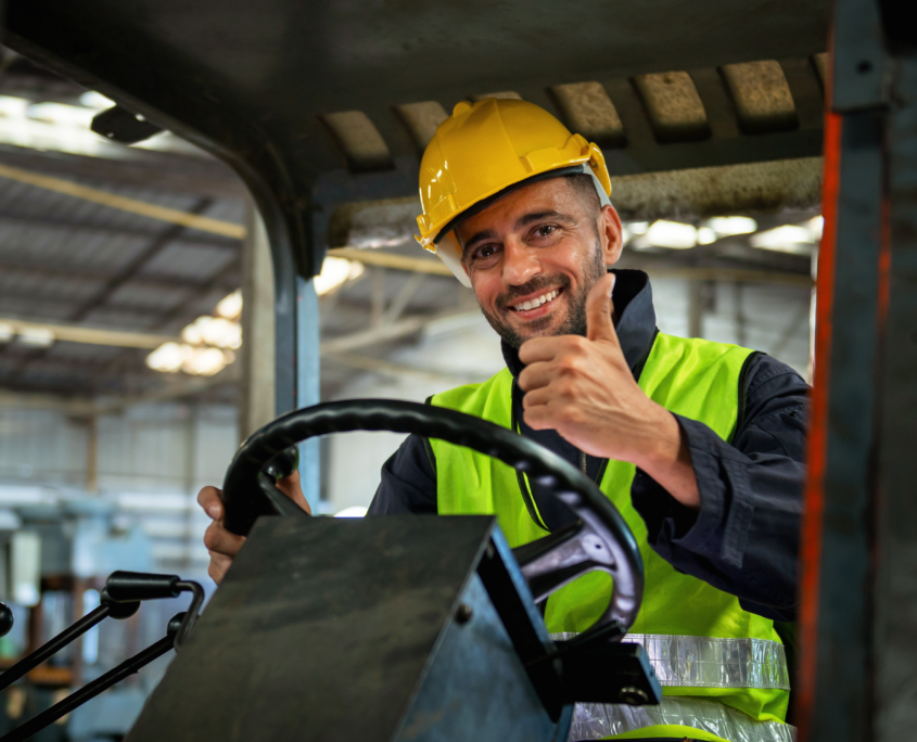 forklift driver sits in his vehicle in a warehouse and gives a thumbs up to show confidence in his work