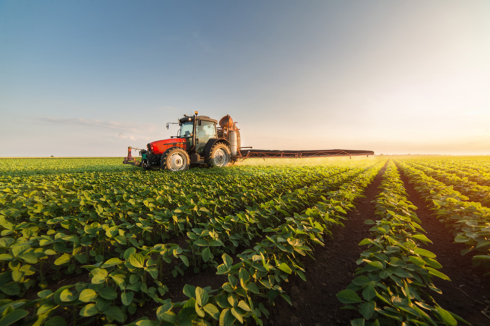 Red agricultural tractor spraying crops across a green field at sunset, representing Baldwin filtration solutions for farming equipment.