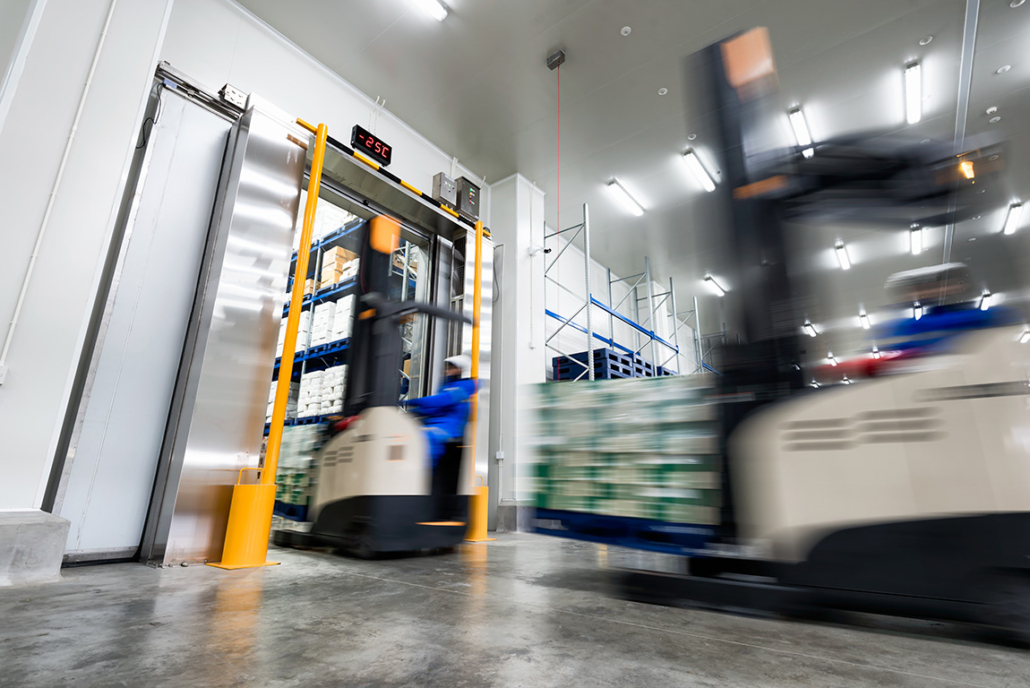 Forklifts transporting palletized goods through an industrial cold storage warehouse with a temperature-controlled loading area.